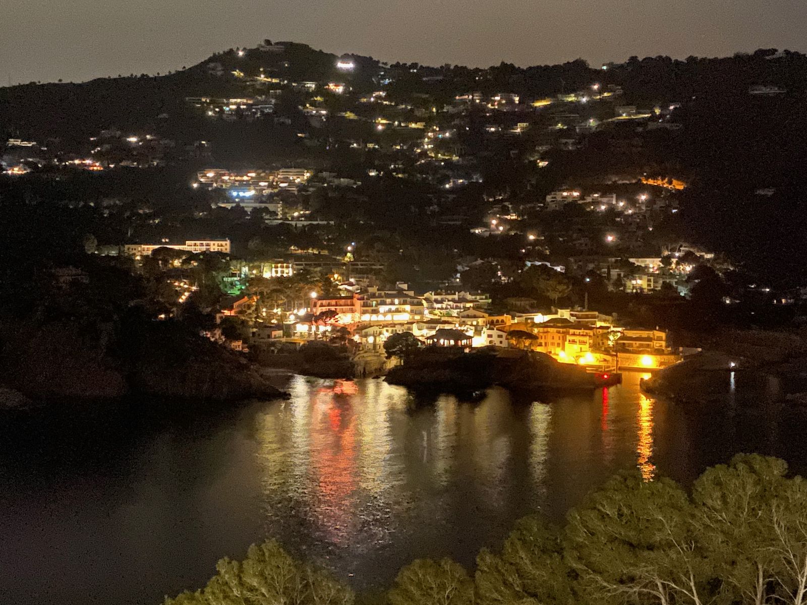 Le hameau illuminé au fond de la crique, la nuit, et ses reflets orange sur l'eau